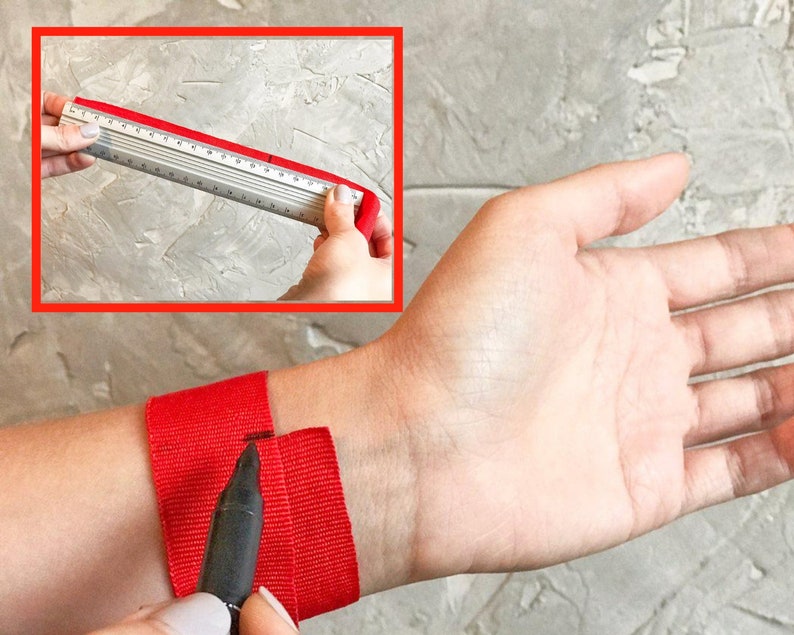 May include: A red fabric wristband is being measured with a ruler. A black marker is being used to mark the fabric.