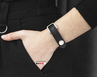 May include: A black leather bracelet with a silver buckle and a silver button closure.
