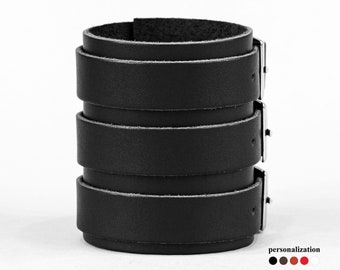 Könnte beinhalten: Schwarzes Lederarmband mit drei verstellbaren Riemen und silbernen Schließen.