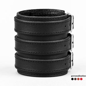 Puede incluir: Pulsera de brazalete de cuero negro con tres correas ajustables y hebillas plateadas.