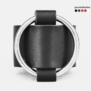 May include: A black leather cuff bracelet with a large, silver-colored metal ring. The bracelet has a simple, modern design. The word "personalization" is in the upper right corner, with color options.