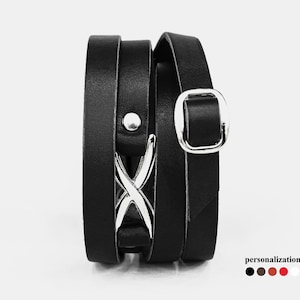 May include: Black leather wrap bracelet with a silver X-shaped accent and a silver buckle. The bracelet is available in black, brown, red, and white.