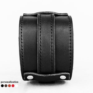May include: A black leather wrist cuff with a wide band and vertical straps. The cuff features white button closures and visible stitching. The word "personalization" is at the bottom, with color options.