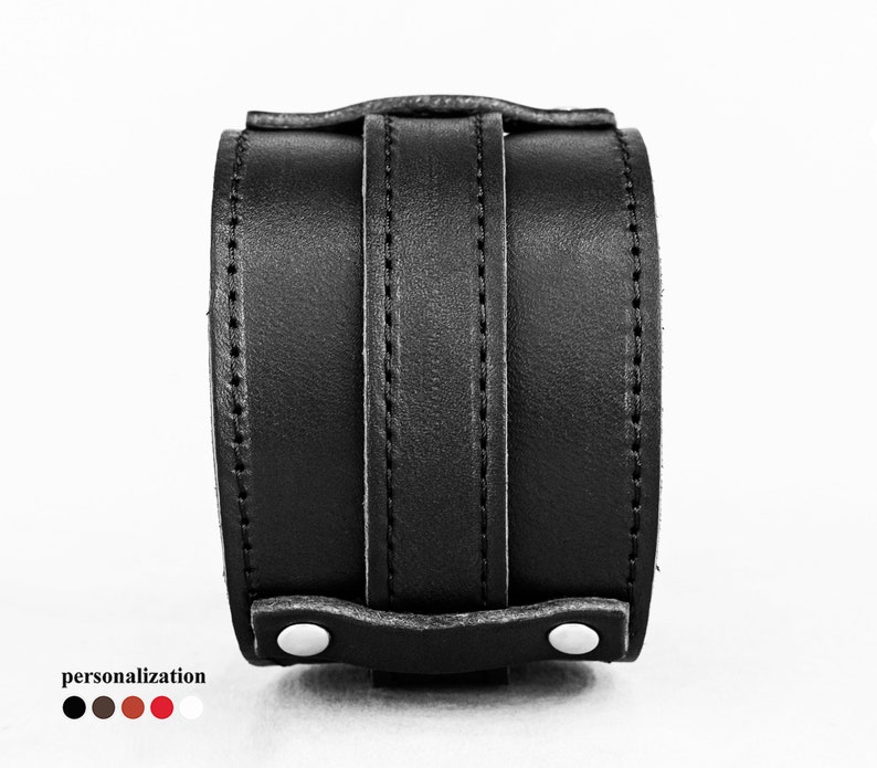 May include: A black leather wrist cuff with a wide band and vertical straps. The cuff features white button closures and visible stitching. The word "personalization" is at the bottom, with color options.