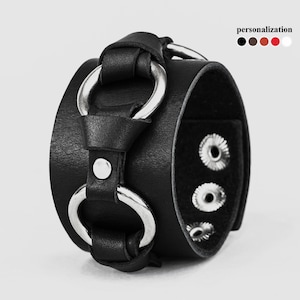 May include: Black leather bracelet with silver metal rings and snap closures.