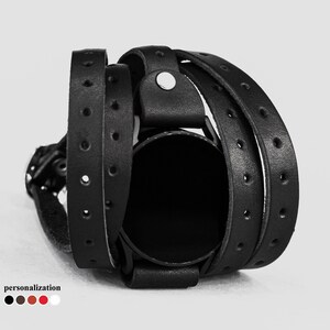 May include: Black leather watch band with a wrap-around design. The band is made of multiple layers of leather and has a simple, minimalist style.