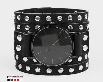 May include: Black leather cuff watch with silver studs. The watch face is black with silver hands.