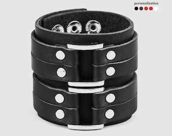 May include: Black leather cuff bracelet with silver metal accents and a buckle closure. The bracelet has three rows of leather and silver studs.