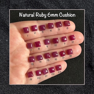 May include: Twenty-three natural ruby gemstones, each measuring 6mm, are displayed on a hand. The rubies are cushion cut and have a deep red colour. The gemstones are arranged in rows, with each row labelled with a number from 1 to 23.