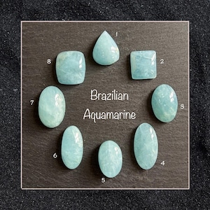 May include: Eight Brazilian aquamarine gemstones in various shapes, including teardrop, square, and oval. The gemstones are a light blue colour and are arranged in a circular pattern. The text "Brazilian Aquamarine" is in the centre.