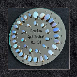 May include: A circular display of 37 Brazilian Opal Doublets, labeled with numbers 1 through 37. The opals are set in a silver-toned metal setting and are arranged in a circle on a mirrored surface. The text "Brazilian Opal Doublets (Lot 3)" is printed in the center of the display.