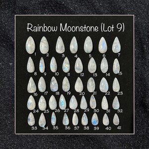 May include: A display of 41 teardrop-shaped Rainbow Moonstone gemstones, numbered 1-41, against a black backdrop. The stones are primarily white with iridescent colour flashes. The text "Rainbow Moonstone (Lot 9)" is at the top.