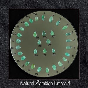 Könnte beinhalten: Nahaufnahme von 32 natürlichen zambischen Smaragden, die in einem Kreis auf einem grauen Hintergrund angeordnet sind. Jeder Smaragd ist von 1 bis 32 nummeriert.