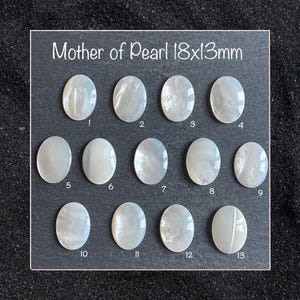 Puede incluir: Una colección de trece cabujones ovalados de nácar, cada uno de aproximadamente 18 x 13 mm, dispuestos sobre un fondo oscuro. El texto "Mother of Pearl 18x13mm" es visible. Cada cabujón presenta un patrón iridiscente único.