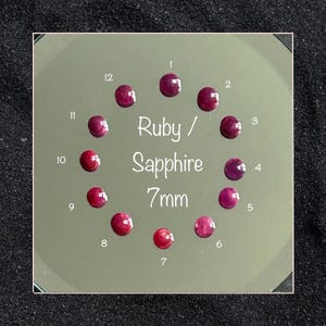 Puede incluir: Doce piedras preciosas de rubí y zafiro redondas de 7mm dispuestas en círculo sobre una superficie reflectante. Cada piedra está numerada del 1 al 12. El texto "Ruby / Sapphire 7mm" está impreso en el centro de la disposición circular.