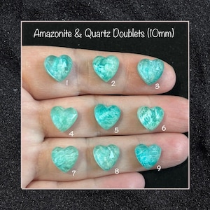 Może przedstawiać: Dziewięć sercowatych dubletów amazonitu i kwarcu, każdy o wymiarach 10 mm, jest prezentowanych na dłoni. Kamienie są jasnozielone i mają błyszczące, tęczowe wykończenie.