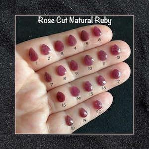 Peut inclure: Vingt pierres précieuses de rubis naturels taillées en rose, numérotées de 1 à 20, sont présentées sur une main. Les pierres précieuses sont de couleur rouge foncé et ont une forme de poire.