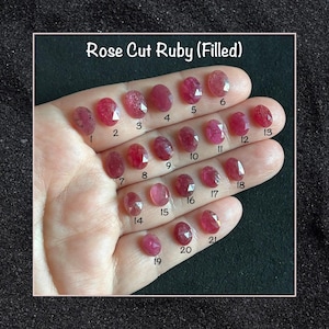 May include: Twenty-one rose cut rubies, numbered 1 through 21, are displayed on a hand. The rubies are a deep red color and have a faceted, oval shape. The rubies are labeled "Rose Cut Ruby (Filled)".