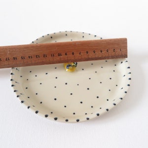 May include: Cream-colored ceramic plate with a blue polka dot pattern and a yellow decorative element. A wooden ruler is placed across the plate, measuring approximately 8 inches in length.