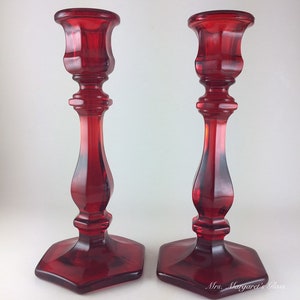 May include: A pair of red glass candle holders with a hexagonal base and a fluted design.