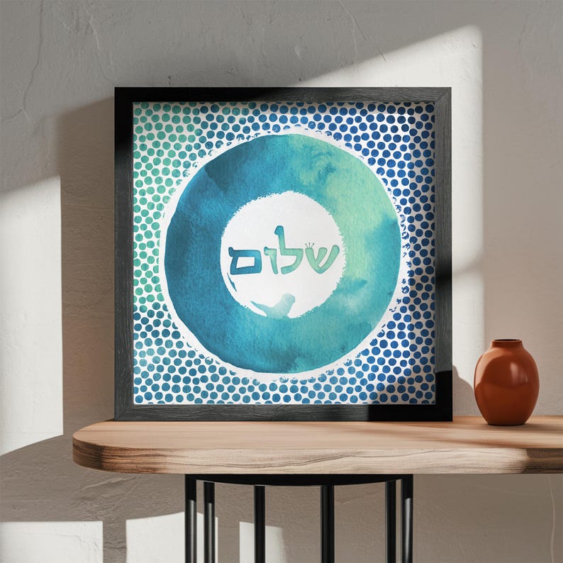 May include: A framed print featuring a blue and green watercolour circle design. The circle contains the Hebrew word "Shalom" written in white. The background is a pattern of blue dots.