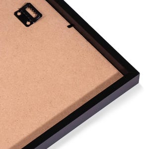 May include: Black picture frame with a brown cardboard backing. The frame has a hanging hook on the back.