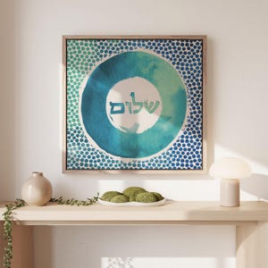 May include: A framed watercolour painting with a blue and green circle design. The circle has a white background with the Hebrew word "Shalom" written in it. The background of the painting is a white and blue polka dot pattern.