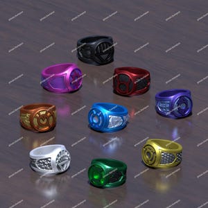 May include: A collection of nine rings in various colors, each with a unique design. The rings include black, purple, red, orange, blue, silver, green, and gold. The rings are displayed on a wooden surface.
