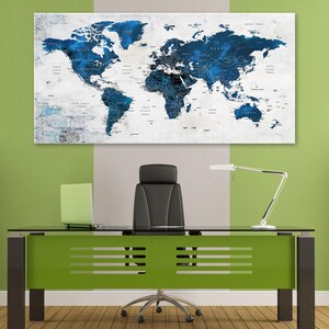 May include: A blue and white world map print hanging on a wall above a green desk with a black office chair. The map is a watercolor style with a white background and blue continents.