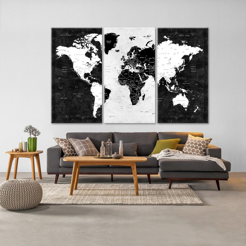 May include: A black and white world map print in three panels, displayed above a gray sectional sofa with a wooden coffee table and a side table. The sofa has a throw blanket and decorative pillows.
