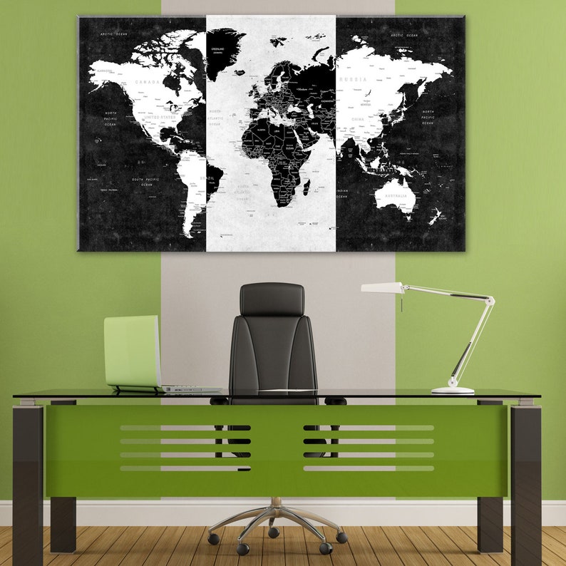 May include: A black and white world map print in three panels hangs on a wall above a glass-top desk with a green base. A black office chair sits in front of the desk. A lamp with a white shade is on the desk.