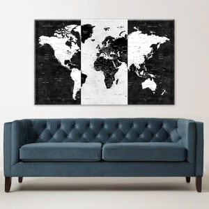 May include: A black and white world map print with a distressed, vintage look. The map is divided into three sections, with the Americas on the left, Europe and Africa in the center, and Asia and Australia on the right. The map is hanging on a white wall above a blue velvet sofa.