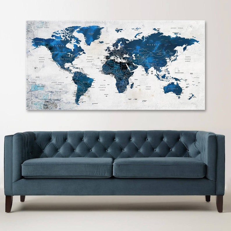 May include: A blue and white world map print with a distressed, textured background. The map is framed and hanging above a blue velvet sofa.