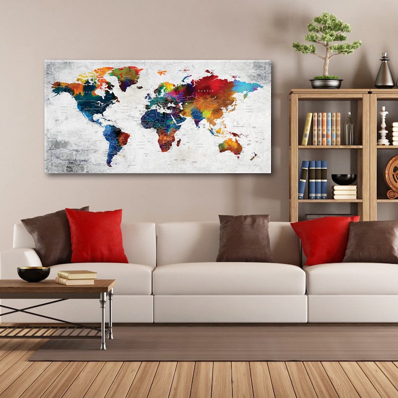 Puede incluir: Una impresi&oacute;n de mapa del mundo colorido con un fondo blanco y una textura desgastada. El mapa est&aacute; pintado en tonos de azul, verde, rojo, naranja y amarillo. El mapa est&aacute; colgado en una pared sobre un sof&aacute; blanco con almohadas rojas y marrones.