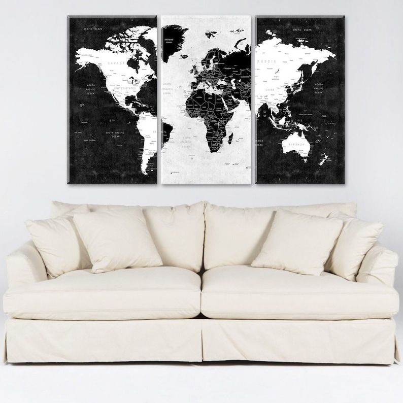 May include: A black and white world map print in three panels, hanging above a white couch with white pillows.