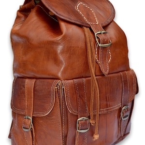 May include: A brown leather backpack with multiple pockets and buckles. The backpack has a drawstring closure and a flap with a buckle. Chestnut Medium.