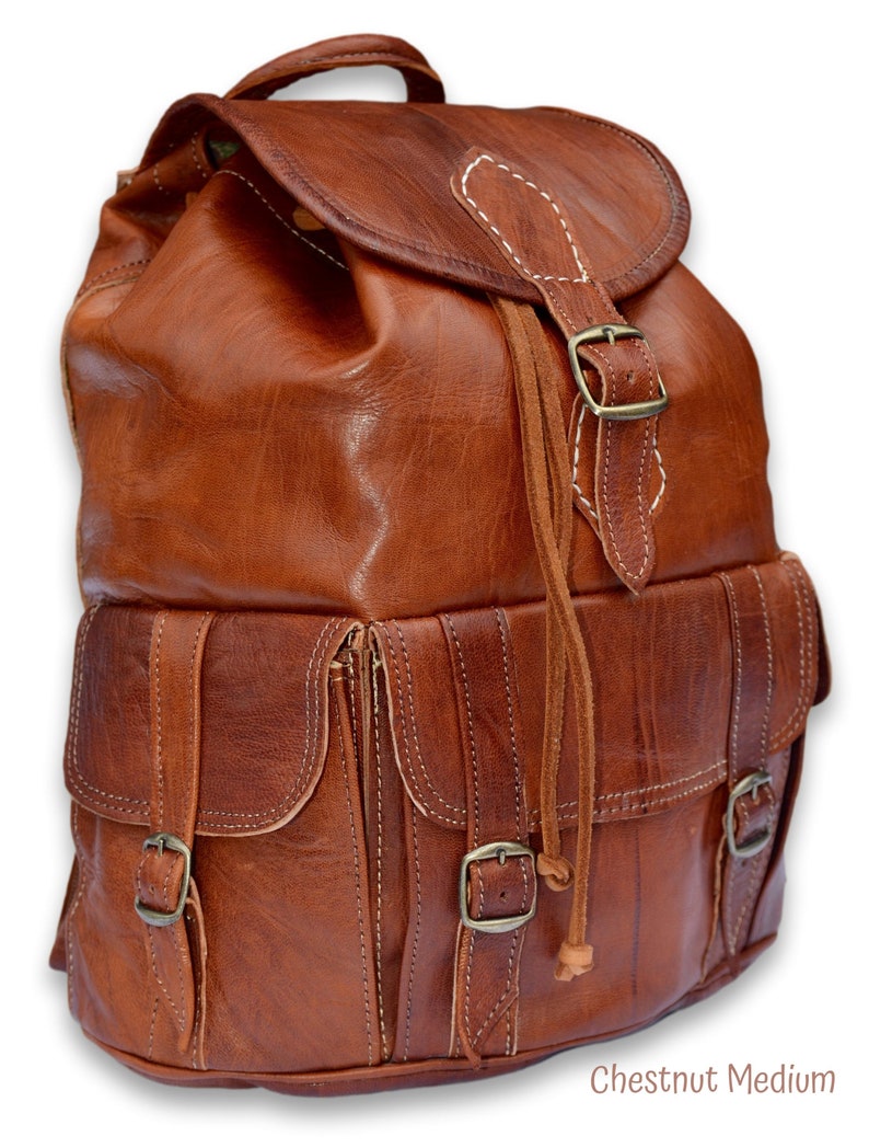 May include: A brown leather backpack with multiple pockets and buckles. The backpack has a drawstring closure and a flap with a buckle. Chestnut Medium.