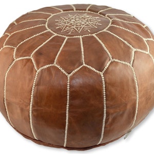 May include: A brown leather pouf with white stitching and a white embroidered star design on the top.