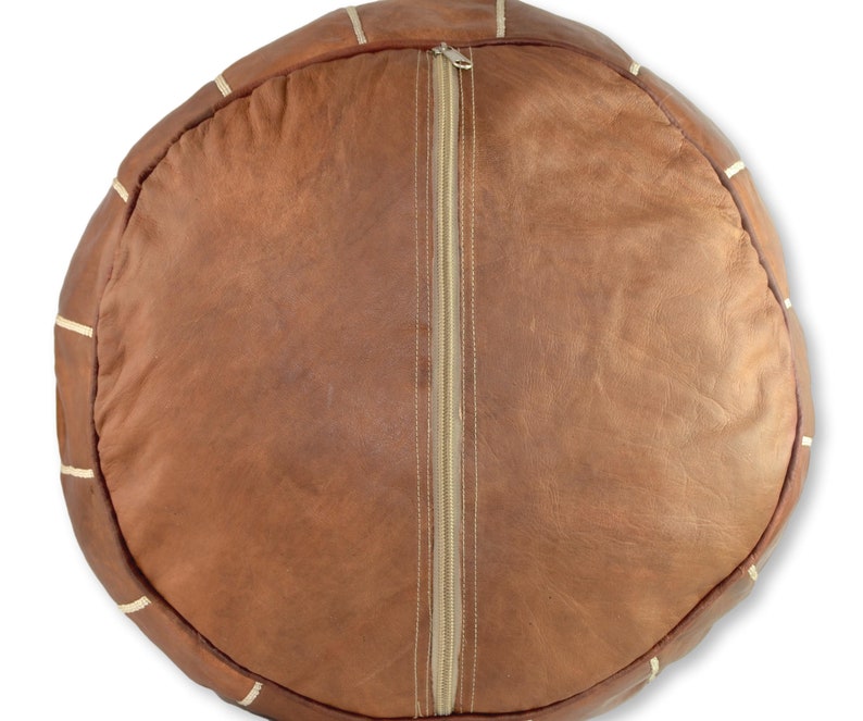 May include: A brown leather pouf with white stitching and a zipper closure. The pouf is round and has a smooth surface.