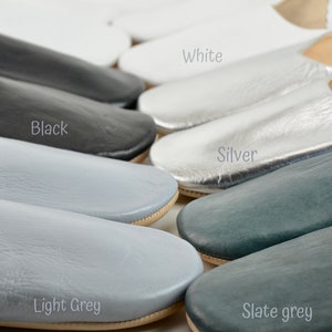 Peut inclure: Une collection de chaussons en cuir de diff&eacute;rentes couleurs, dont blanc, noir, argent, gris clair et gris ardoise. Les chaussons ont un design simple &agrave; enfiler avec un bout arrondi et une semelle de couleur neutre. L'image inclut les noms des couleurs.