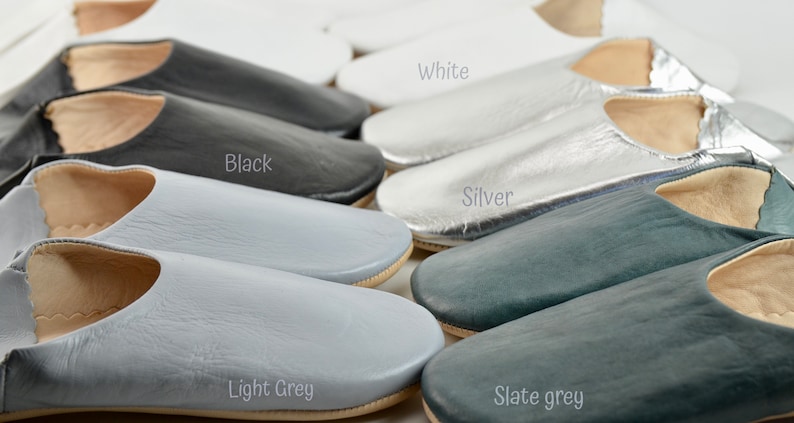 Peut inclure: Une collection de chaussons en cuir de diff&eacute;rentes couleurs, dont blanc, noir, argent, gris clair et gris ardoise. Les chaussons ont un design simple &agrave; enfiler avec un bout arrondi et une semelle de couleur neutre. L'image inclut les noms des couleurs.