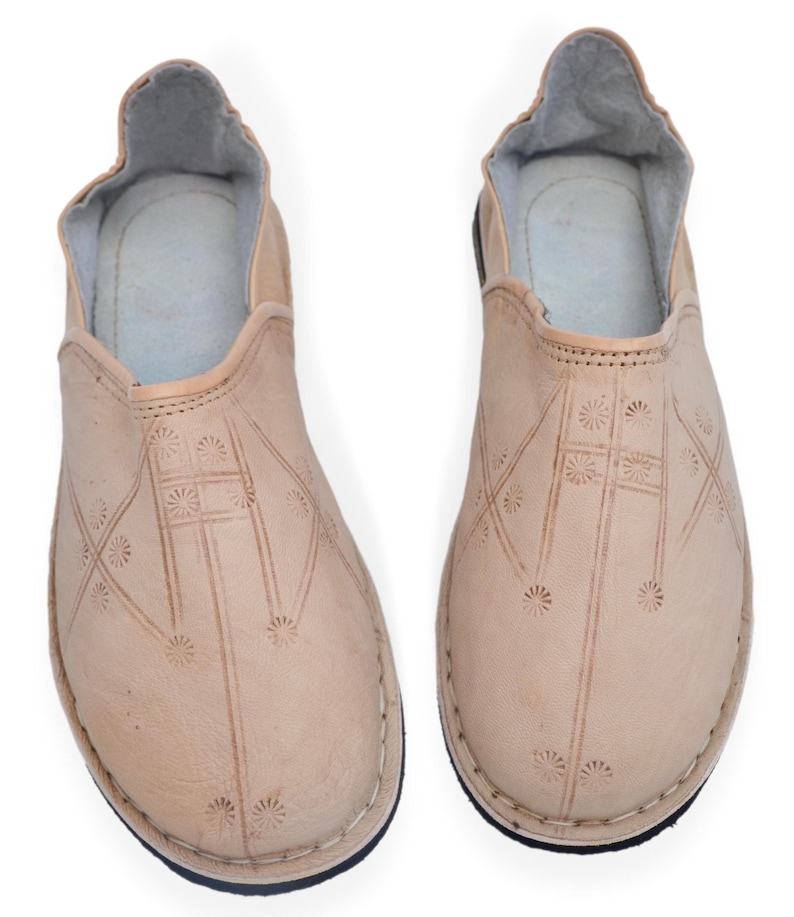 May include: A pair of light beige slip-on shoes featuring a rounded toe and a low-cut opening. The exterior surface is decorated with a repeating pattern of small, stamped sunburst motifs connected by thin, straight lines across the vamp.