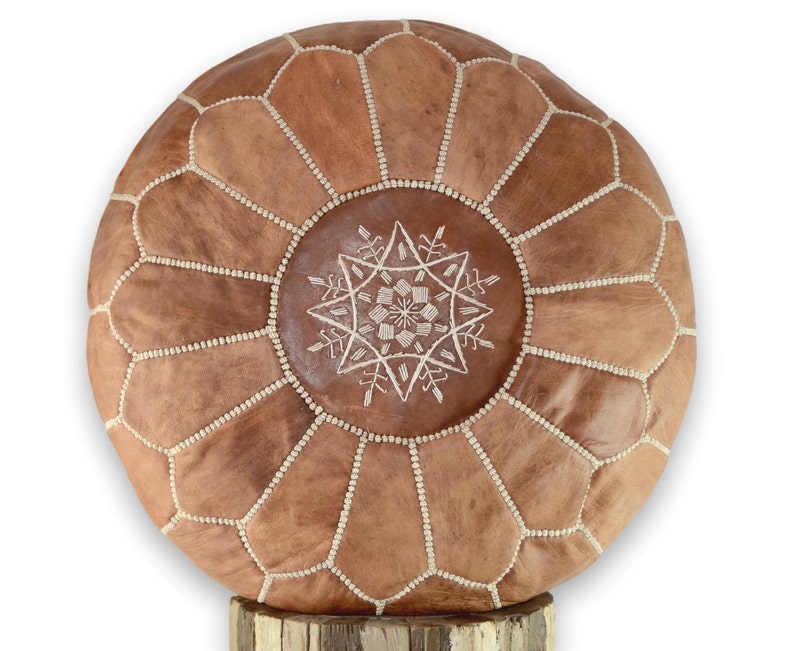 May include: A round brown leather pouf with white stitching and a white embroidered star design.