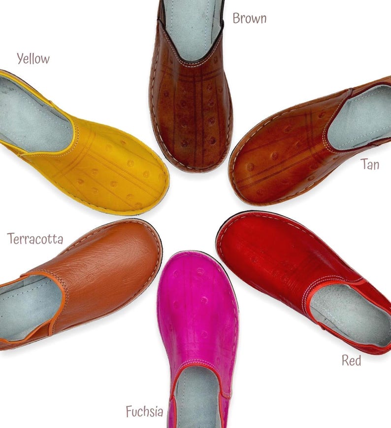 May include: Six slip-on shoes arranged in a circle, each featuring a distinct color: yellow, brown, tan, terracotta, fuchsia, and red. Each shoe has a smooth, rounded toe, visible stitching along the edges, and a light-colored interior lining.