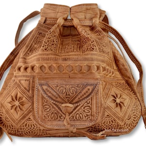May include: A brown leather drawstring bag with intricate embossed patterns and a smaller pocket on the front. The bag has a long strap and a tassel.