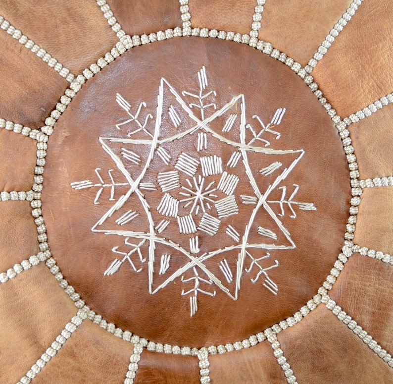 May include: A brown leather pouf with a white embroidered star design.