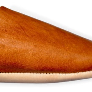 Peut inclure: Gros plan d'une pantoufle en cuir marron. La chaussure a un bout arrondi et une semelle de couleur claire. Le cuir a un aspect textur&eacute; et une couleur chaude et naturelle. La semelle est cousue &agrave; la tige.