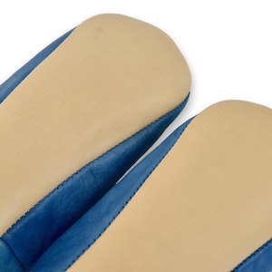 Peut inclure: Gros plan sur deux chaussons en cuir bleu avec des semelles beiges. Les chaussons ont une couture cousue sur les bords. Les semelles sont de couleur beige clair et le cuir est bleu vif.