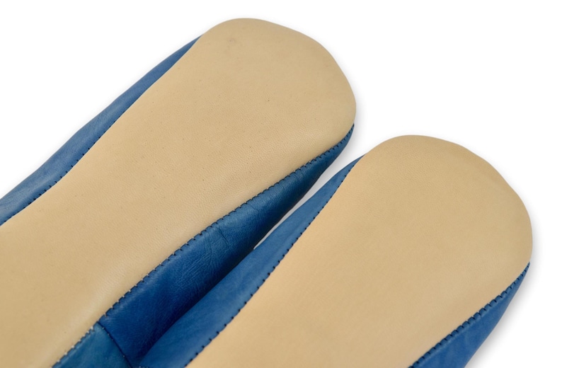 Peut inclure: Gros plan sur deux chaussons en cuir bleu avec des semelles beiges. Les chaussons ont une couture cousue sur les bords. Les semelles sont de couleur beige clair et le cuir est bleu vif.