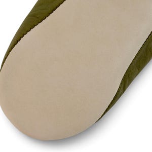 May include: A close-up view of the sole of a shoe, featuring a smooth, light beige leather bottom panel stitched to an olive green leather upper section. The stitching is visible along the seam where the two distinct leather pieces meet.